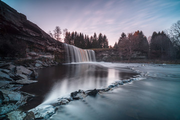 Long exposure photo of Jägala waterfall, 8 meters high and more than 50 meters wide fall in the lower course of the Jägala River. Estonia, Europe. Low sun casts various colors on the water.
