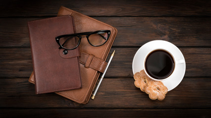 notebooks, glasses and cup of coffee with cookies on a wooden background