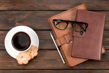 .notebooks, glasses and cup of coffee with cookies on a wooden background