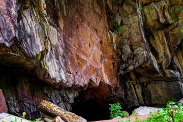 Eingang zu einer Höhle in altem, bunten Gestein bei einer Felswand