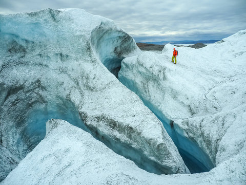 Person in red jacket walking through deep icy crevasse inside glacier with striking blue walls
