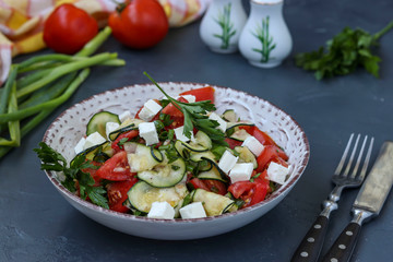 Healthy salad with zucchini, tomatoes and feta, dressed with olive oil in a plate on a dark background, horizontal orientation
