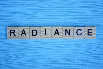 word radiance made of small wooden letters on a light blue paper background