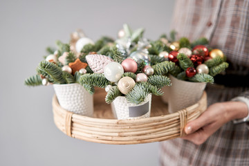 Fototapeta na wymiar Florist holds a tray with christmas arrangements. Beautiful festive arrangement of fresh spruce in coffee Cup. Christmas mood.