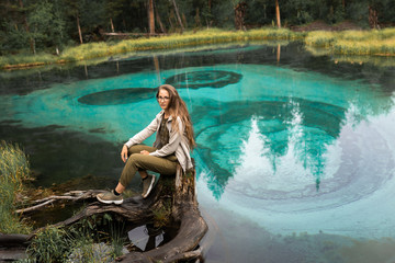 Fototapeta na wymiar A beautiful girl sits on a very beautiful and turquoise geyser lake in Russia, in the Altai Republic. National Reserve. Aqua Menthe color. Mixed forest with pines and cedars