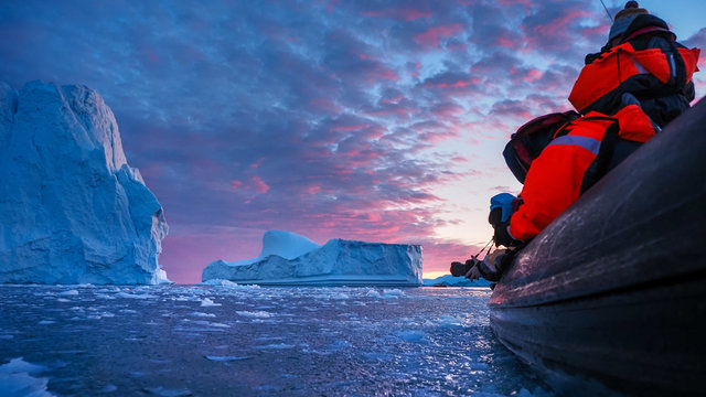 Photographer abd iceberg at sunset. Nature and landscapes of Greenland. Disko bay. West Greenland. Summer Midnight Sun and icebergs. Big blue ice in icefjord. 