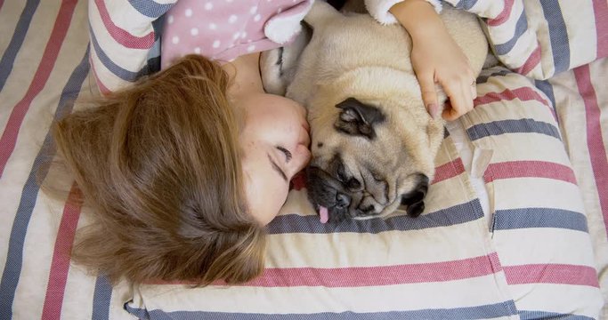 Adorable teen girl and her pug dog in the bed are sleeping together.  Friendship with pet concept. Together forever, inseparable friends