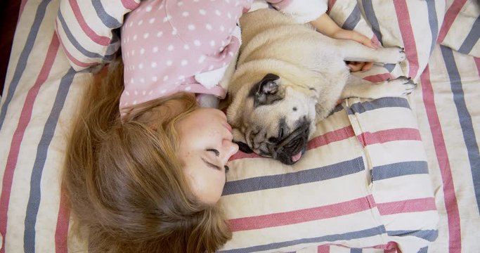 Adorable teen girl and her pug dog in the bed are sleeping together.  Friendship with pet concept. Together forever, inseparable friends
