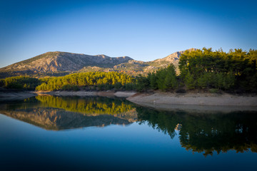 Natural lake surrounded by pine trees, mountains and a village.