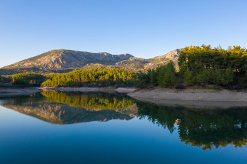 Fototapeta premium Natural lake surrounded by pine trees, mountains and a village.