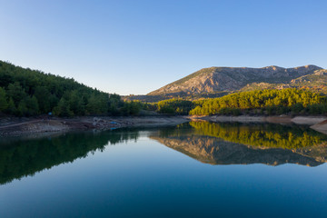 Fototapeta premium Natural lake surrounded by pine trees, mountains and a village.
