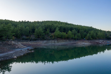 Natural lake surrounded by pine trees, mountains and a village.