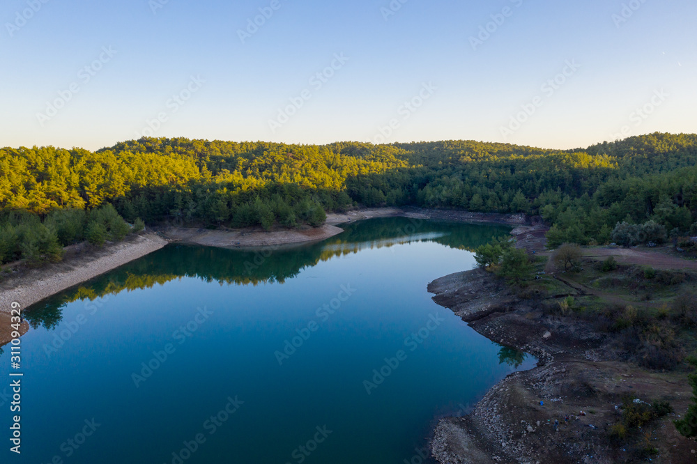 Wall mural natural lake surrounded by pine trees, mountains and a village.