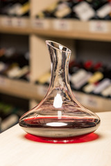 decanter with red wine, in the background a rack of wine bottles, the background is blurred