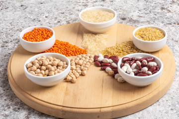 Set of raw legumes, beans, chickpeas, lentils and cereals, rice and bulgur on a wooden tray on a gray background. Healthy food, Protein source for vegetarian.