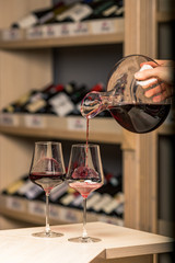 decanter with red wine, in the background a rack of wine bottles, the background is blurred