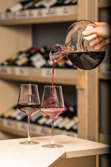 decanter with red wine, in the background a rack of wine bottles, the background is blurred