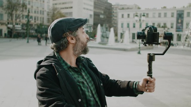 Social media influencer filming himself talking to camera in urban environment.Making of of a shoot where an adult male is using camera gear to film his social media show or video in a European city.