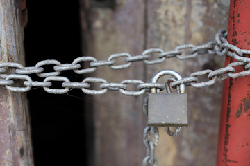A chain of silver color with closed padlock on an old gate. Closeup of old wooden door with closed padlock on a chain.