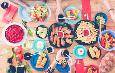 Top view of group of people having dinner together while sitting at wooden table. Food on the table. People eat fast food.