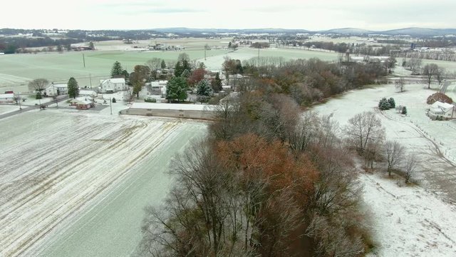 Idyllic winter landscape in rural American countryside, Lancaster County, Pennsylvania in first snow, aerial view of farm next toa small river