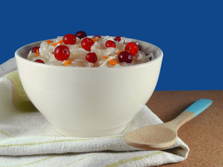 Homemade sauerkraut with cranberries in white bowl on linen napkin next to bamboo wooden spoon on blue background    