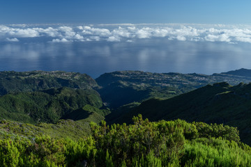 Clouds reflecting from the ocean water during sunrise in Portuguese island Madeira. View from Pico Ruivo path towards Sao Jorge over the dark green slopes of the high mountain array.