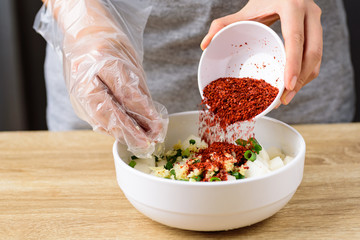 Kimchi radish cooking step 4; pouring cayenne pepper and mixing with sliced spring onion, ginger, garlic and radish in a bowl