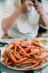Close up of a dish full of red crabs with a mid section of human grabbing and eating with hands  