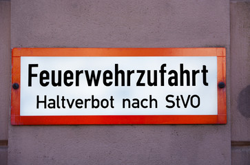 A red and white sign on a red, with the words "Feuerwehrzufahrt. Haltverbot nach StVO", translation: Driveway for fire brigade, Absolute stopping restriction, in black letters.