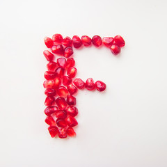 letter F folded from pomegranate berries on a white background top view