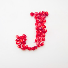 letter J folded from pomegranate berries on a white background top view