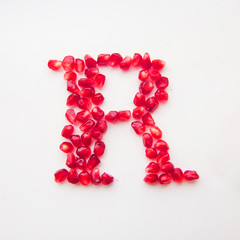 letter R folded from pomegranate berries on a white background top view