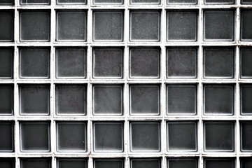 Repetitive texture with identical gray squres, a rectangular pattern of square glass tiles, dark and dusty, high contrast image.