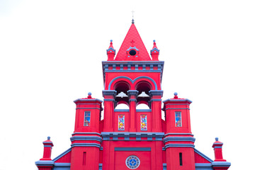 A red church tower and spire with bells, isolated on pale sky background.