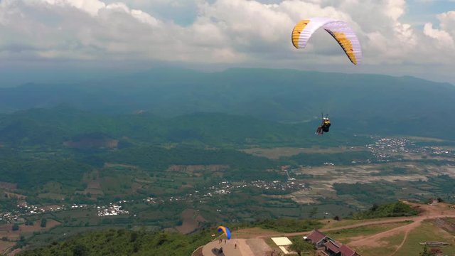 Amazing aerial video of flying paraglider on the background of wild nature. Paraplan drifting above the green tropical trees. Extreme sport. Hipster modern hobby concept. Paraplane flying in the sky.