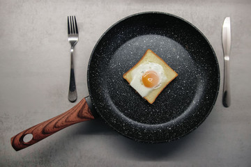 baked egg inside toast bread in a black pan with a fork and knife on the sides top view