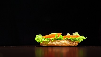 Craft burger is cooking on black background in black food gloves. Consist: sauce, lettuce, tomato,...