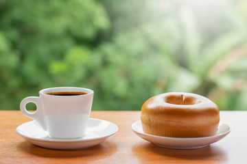 In the morning people wake up and drink coffee before going to work or travel. The espresso coffee in a white cup. All on the table The backdrop to the green nature.  Y