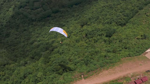 Amazing aerial video of flying paraglider on the background of wild nature. Paraplan drifting above the green tropical trees. Extreme sport. Hipster modern hobby concept. Paraplane flying in the sky.