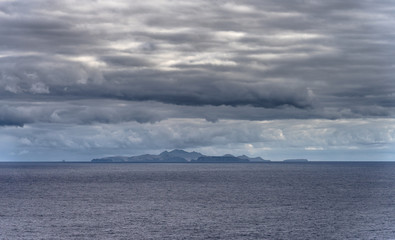 Heavy clouds over Portuguese island Porto Santo northeast of Madeira in Atlantic Ocean during sunrise in the autumn. Rocky volcanic coastline seen from Sao Lourenco peninsula.