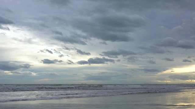 Time lapse, storm clouds pass through the sky with golden lights of the sun during sunset on a beach with the sea breaking against the sand