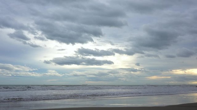 Storm clouds pass through the sky with golden lights of the sun during sunset on a beach with the sea breaking against the sand