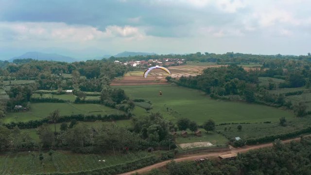 Amazing aerial video of flying paraglider on the background of wild nature. Paraplan drifting above the green tropical trees. Extreme sport. Hipster modern hobby concept. Paraplane flying in the sky.