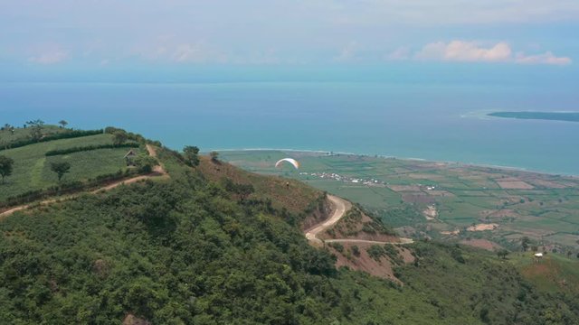 Amazing aerial video of flying paraglider on the background of wild nature. Paraplan drifting above the green tropical trees. Extreme sport. Hipster modern hobby concept. Paraplane flying in the sky.