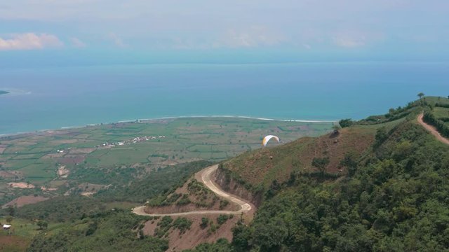 Amazing aerial video of flying paraglider on the background of wild nature. Paraplan drifting above the green tropical trees. Extreme sport. Hipster modern hobby concept. Paraplane flying in the sky.