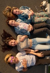 top view of four smiling teenagers lying with their legs on a bench in square at sunset