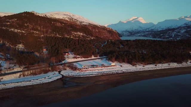 Vanlifers and campers staying at north Norvegian fjord beach. Snowy mountains are in backgraund and arctic sea in front. Aerial backward reveal shot.