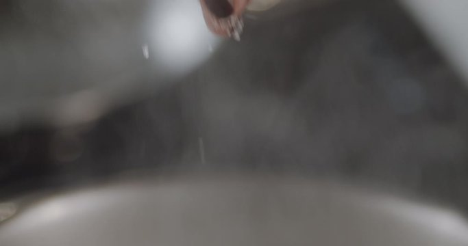 Female chef's fingers sprinkling salt at water. Cookery process. Female adds spice in boiled water in pan. Preparing dishes process in slow motion in restaurant kitchen.