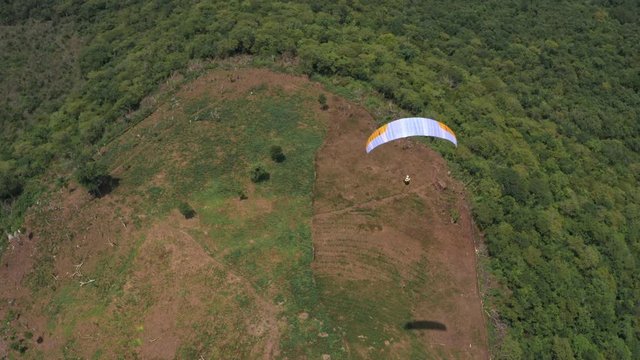 Amazing aerial video of flying paraglider on the background of wild nature. Paraplan drifting above the green tropical trees. Extreme sport. Hipster modern hobby concept. Paraplane flying in the sky.